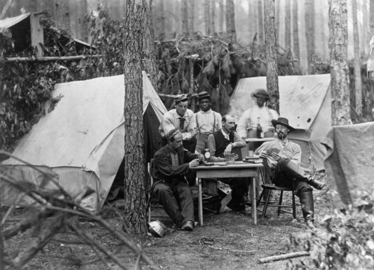 Confederate soldiers playing cards at a table set up outside a tent